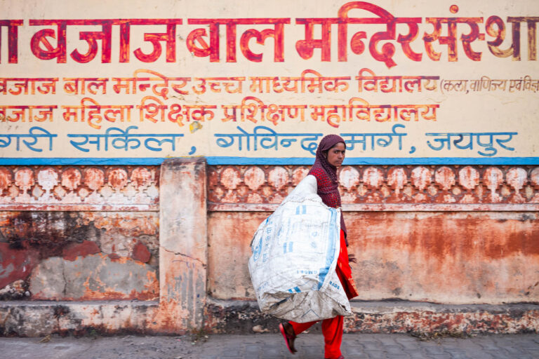 Femme en sari rouge portant un sac d'ordures - Mur décrépit avec lettrage hindou - Reportage quotidien urbain - Agence Brunet-Monié