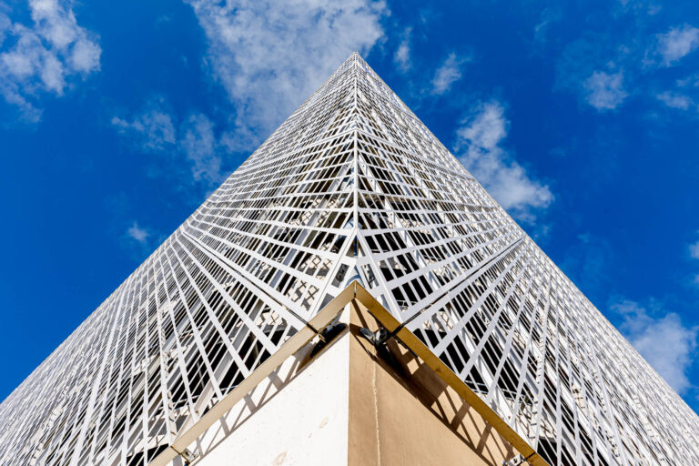 Angle de bâtiment en résille vu du sol - Perspective dynamique vers ciel bleu - Photographie d’architecture professionnelle - Brunet-Monié