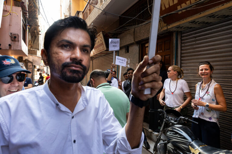 Guide tenant une pancarte - Groupe de visiteurs dans une ruelle indienne - photographie d’une convention en Inde - prestataire photo nantes