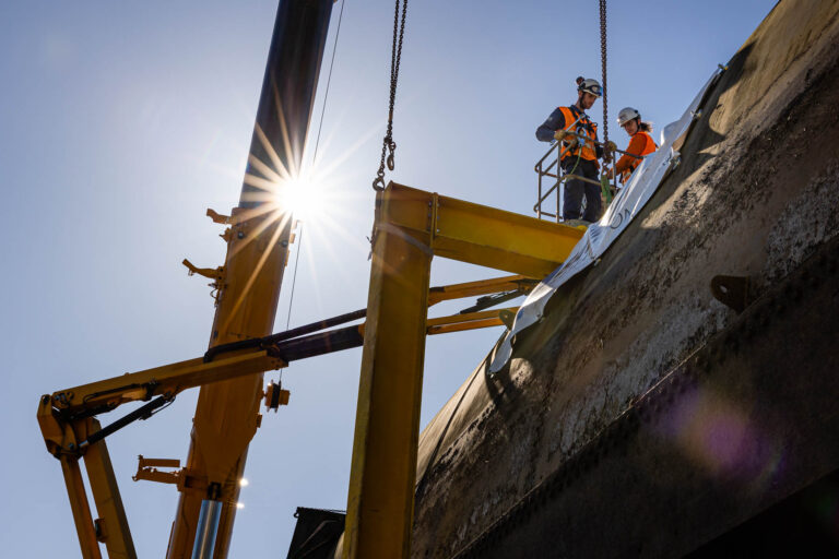 Ouvriers en nacelle au lever de soleil - Grue fixée à pièce métallique imposante - Reportage sur site technique - Agence photo à Nantes