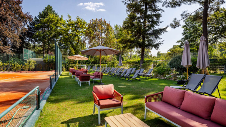 Salon de jardin près d’un court en terre battue - Chaises longues et parasols en plein air - Reportage architecture de club privé - Agence Brunet-Monié
