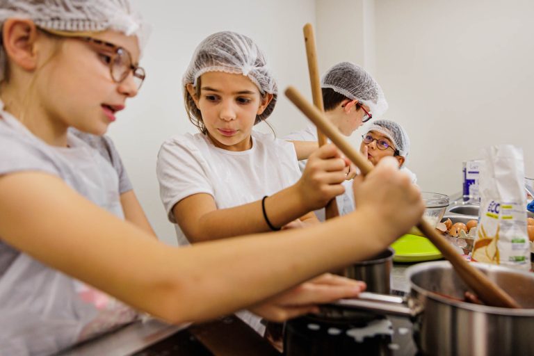Fille remuant casserole en cuisine - Groupe d’enfants concentrés atelier culinaire - photographie colonie vacances - studio photo loire-atlantique