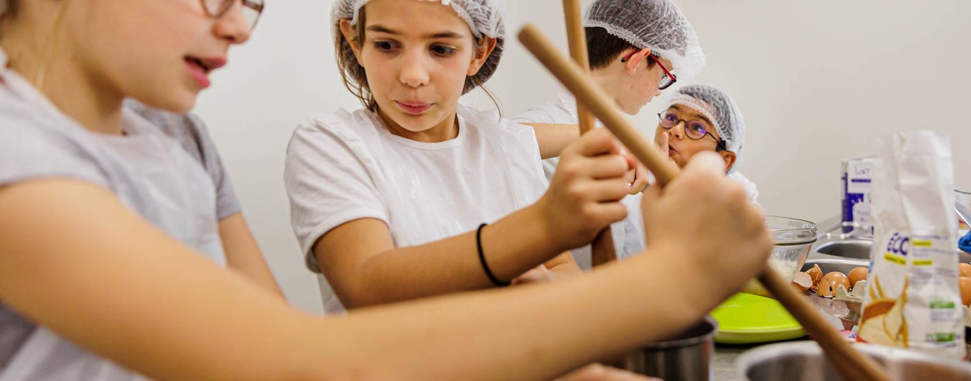 Fille remuant casserole en cuisine - Groupe d’enfants concentrés atelier culinaire - photographie colonie vacances - studio photo loire-atlantique